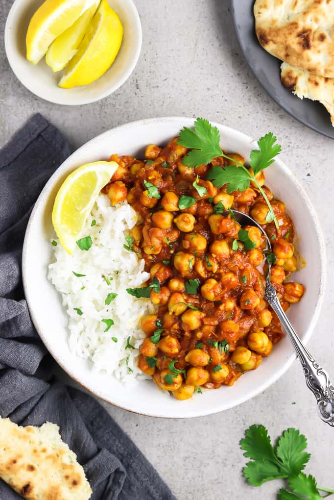 Overhead view of chana masala in a white bowl alongside rice. Garnished with a lemon wedge and cilantro. 