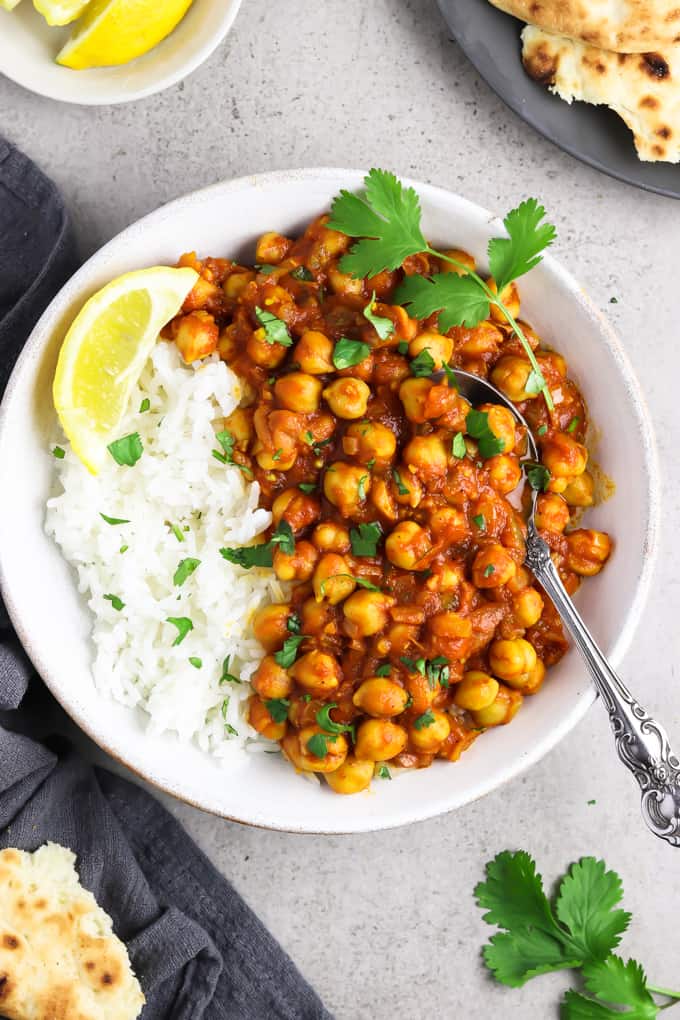 Overhead view of easy chana masala in a white bowl with naan and lemon on the side. 