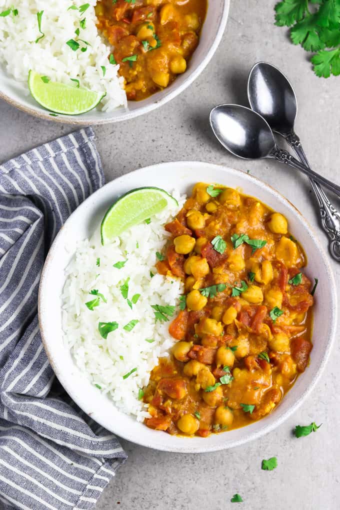 Two white bowls of vegan chickpea curry, topped with cilantro and lime wedges.