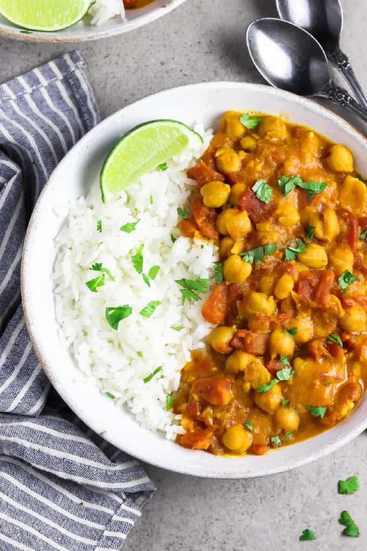 This is the easiest Vegan Chickpea Curry you'll ever make! It calls for pantry staples and it takes 30 minutes on the stove. Plus, it's full of mouth-watering flavor and it's all made in one pan, too! Close up view if a bowl of vegan curry with spoons on the side.