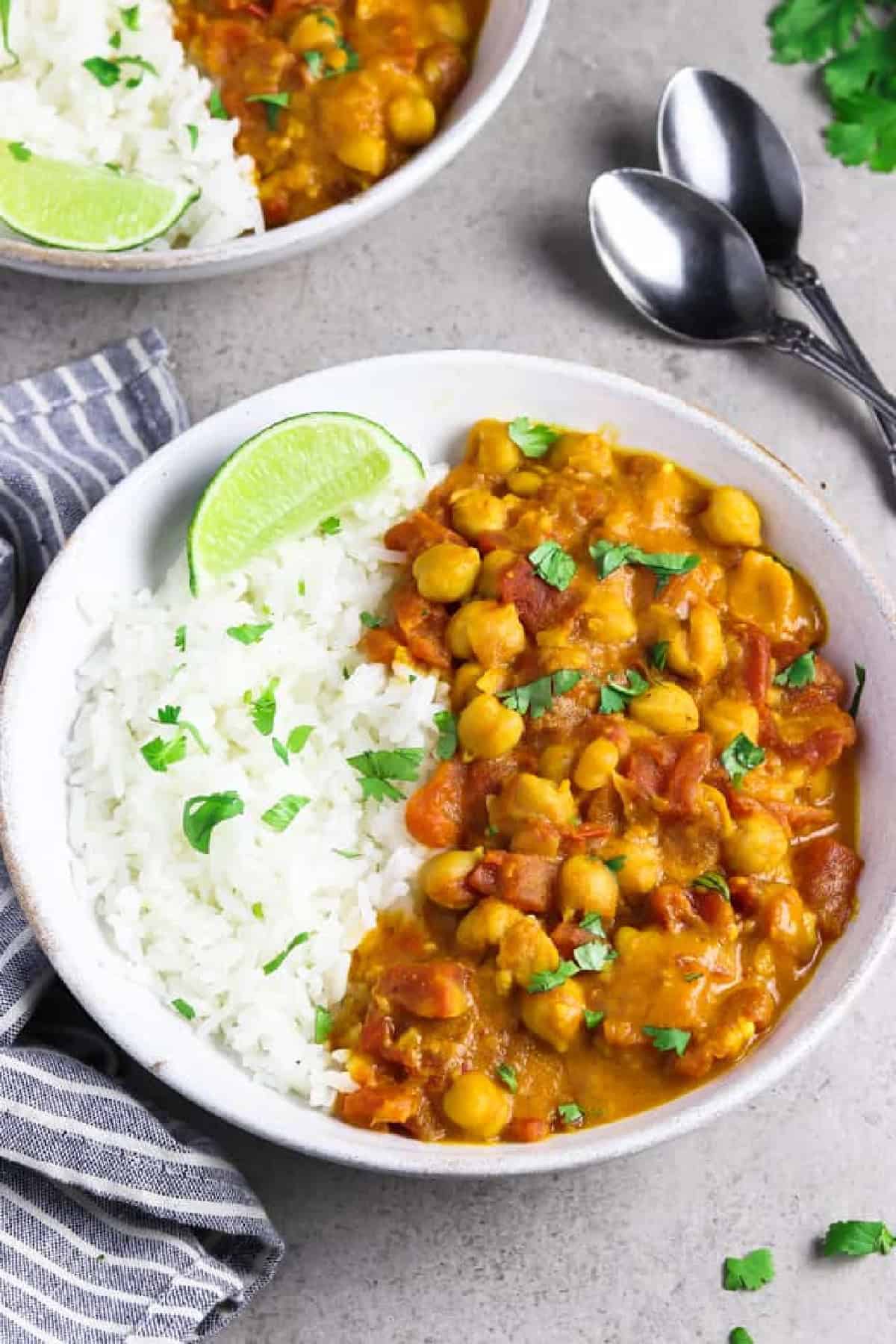 This is the easiest Vegan Chickpea Curry you'll ever make! It calls for pantry staples and it takes 30 minutes on the stove. Plus, it's full of mouth-watering flavor and it's all made in one pan, too! Vegan chickpea curry in a white bowl with a striped napkin on the side.