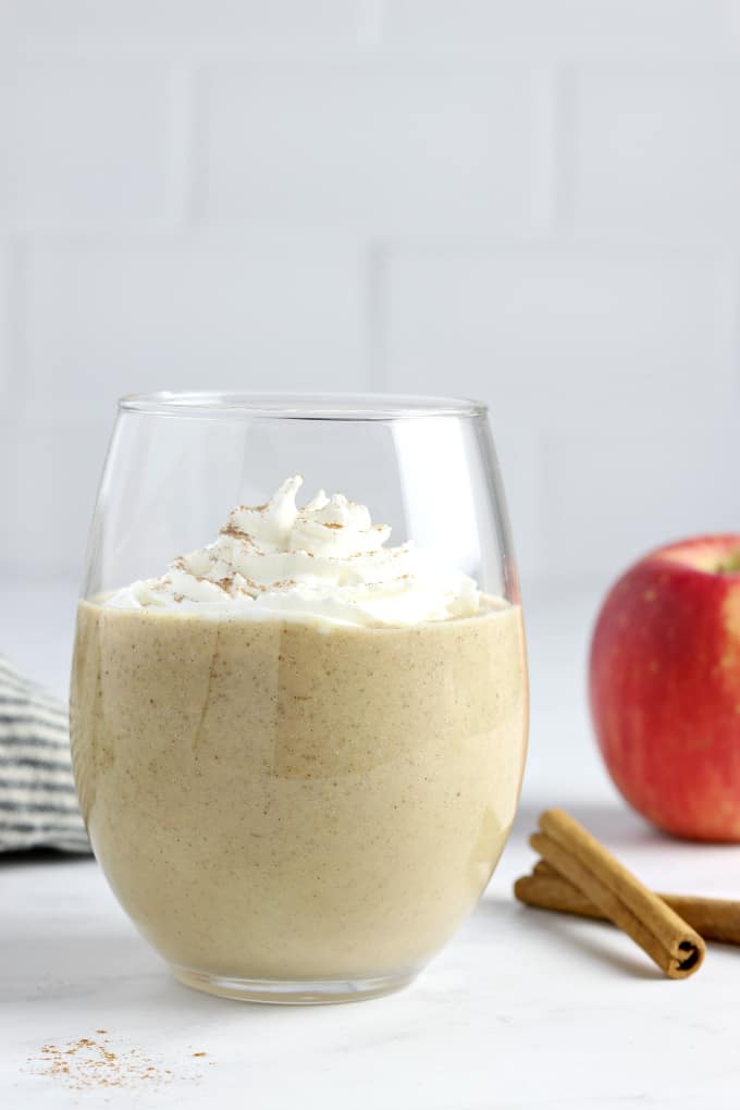 an apple pie smoothie in a glass, topped with whipped cream and cinnamon. 