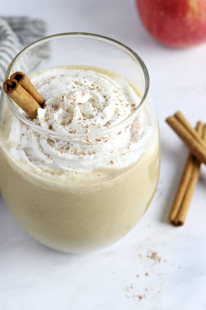 Overhead view of an apple pie smoothie in a glass. Topped with a cinnamon stick and whipped cream.