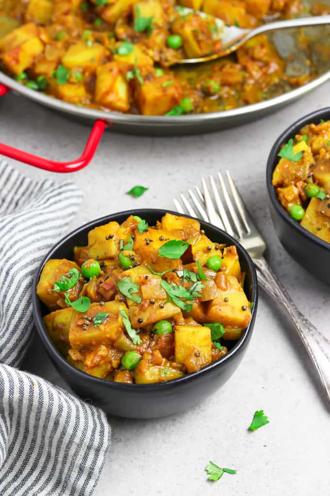 Two bowls filled with bombay potatoes with forks in the middle. 