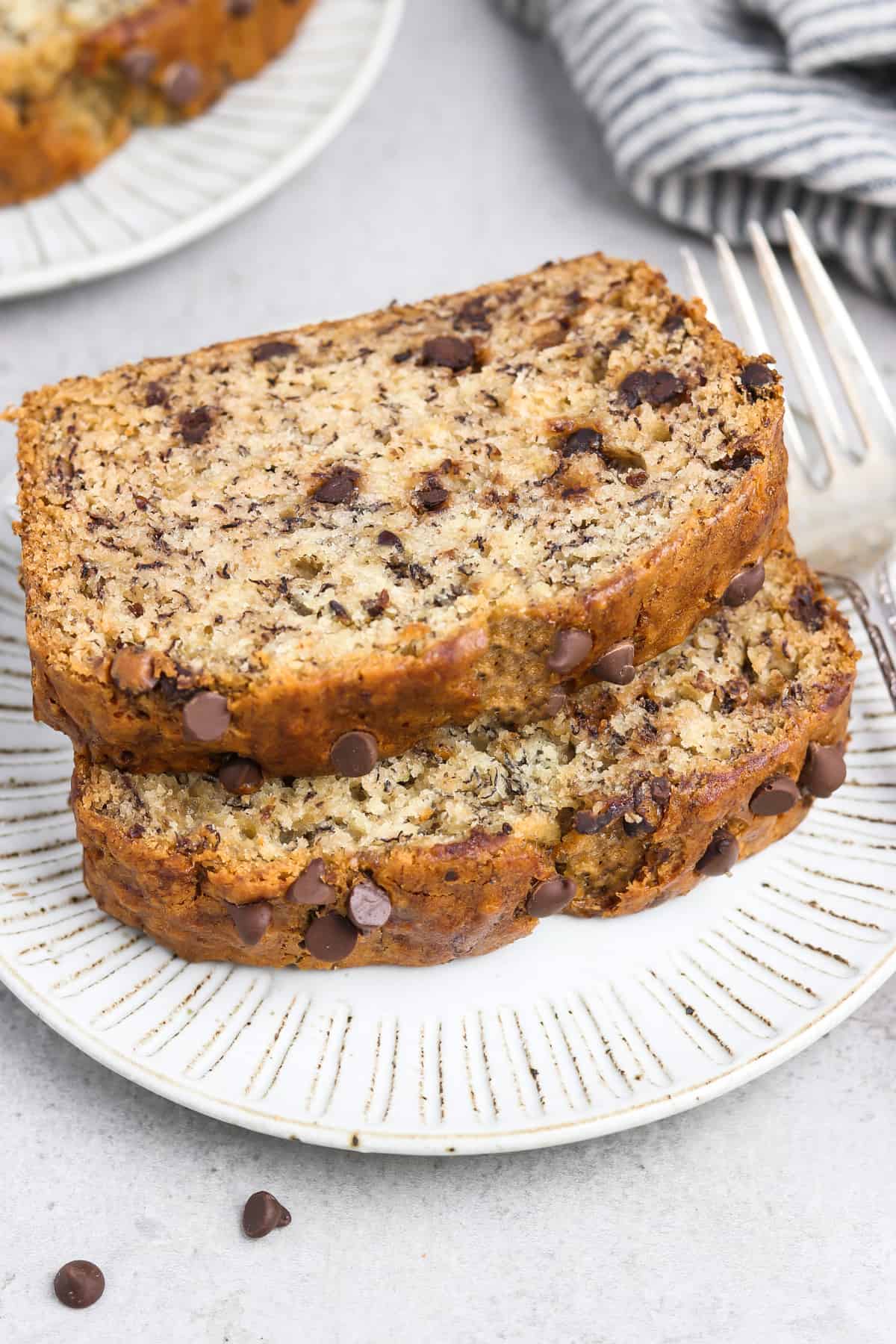 Two slices of banana bread on a white plate with a fork on the side. 