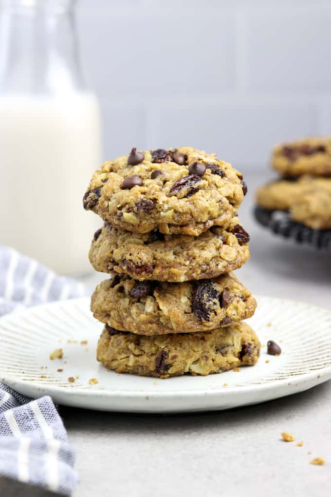 Stack of Oatmeal Raisin Chocolate Chip Cookies on a white plate. Bottle of milk in the background. 