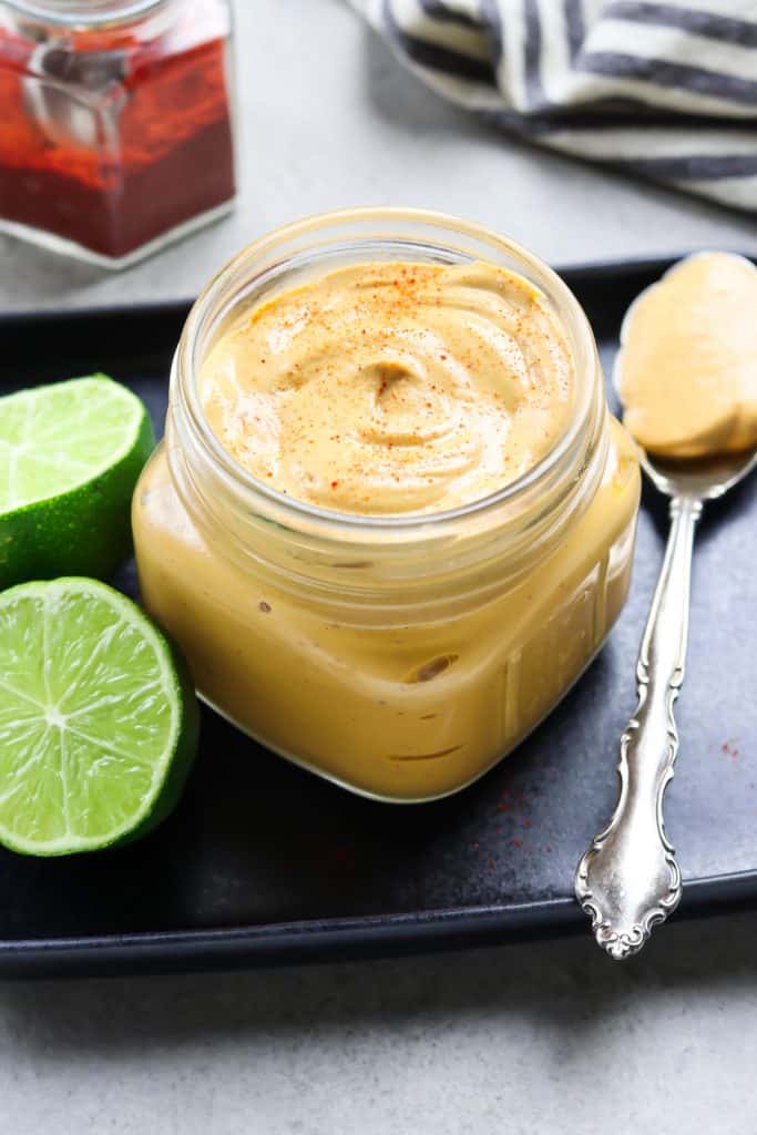 Chipotle sauce in a jar on a black plate. Lime and spoon on the side.