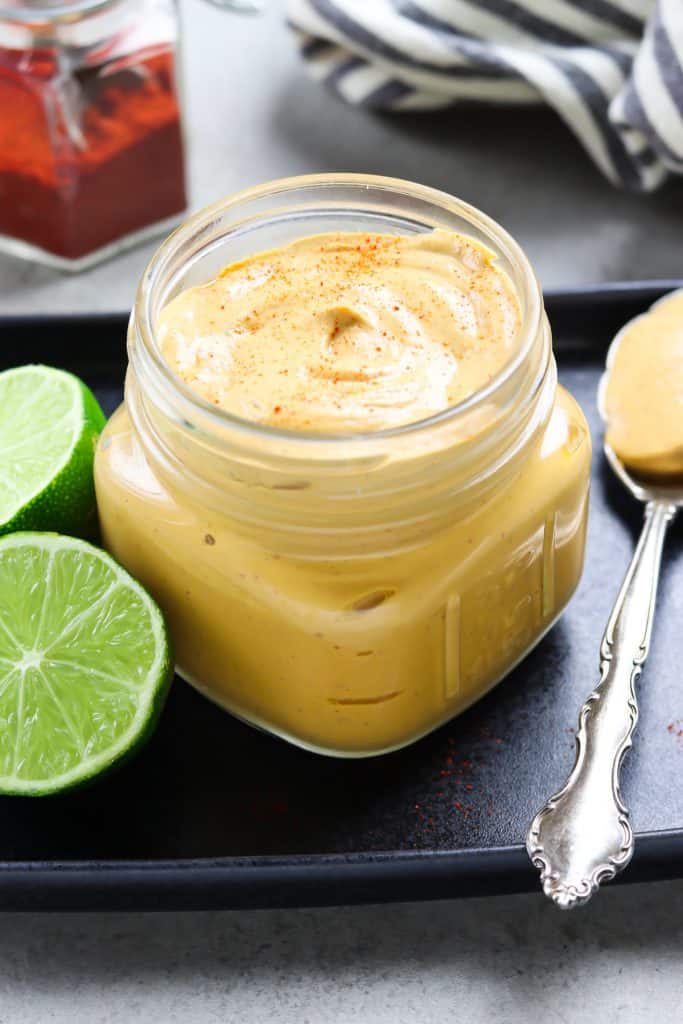 Overhead view of creamy chipotle sauce in a jar with limes and spoon on the side. 