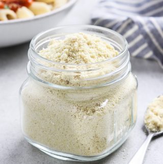 vegan parmesan in a glass jar and spoon on the side.