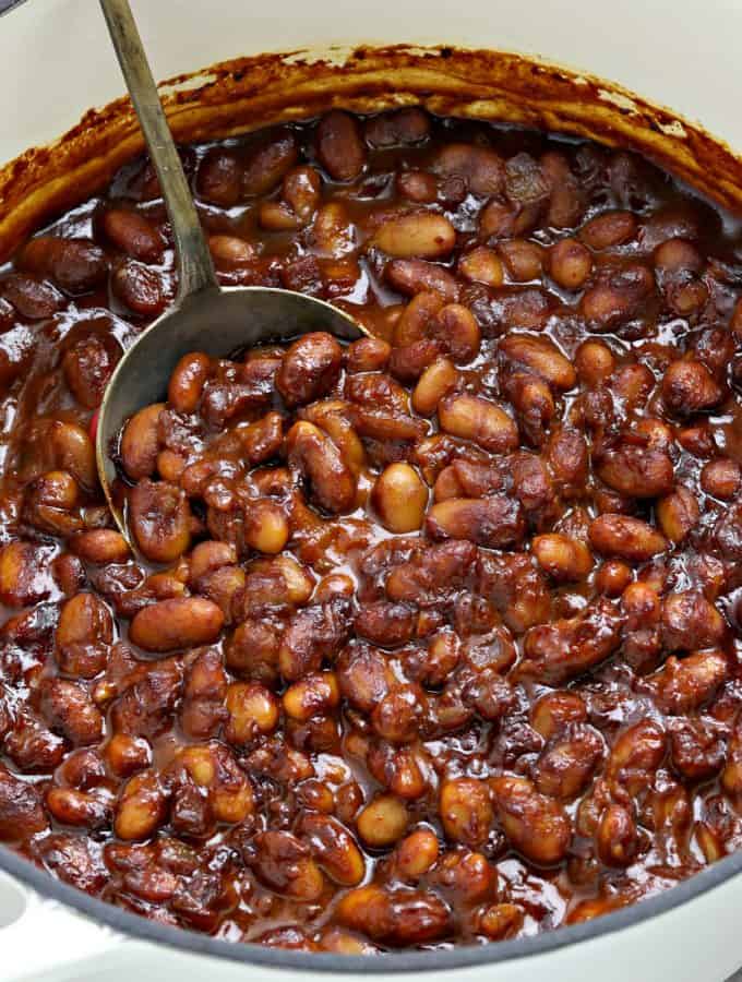 fully cooked beans in a white pot with a spoon in the middle.