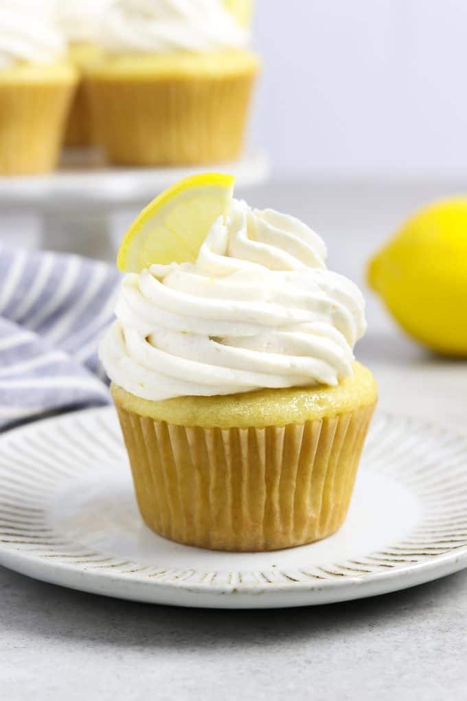 one frosted cupcake on a white plate. Lemon cupcakes on a stand in the background. 