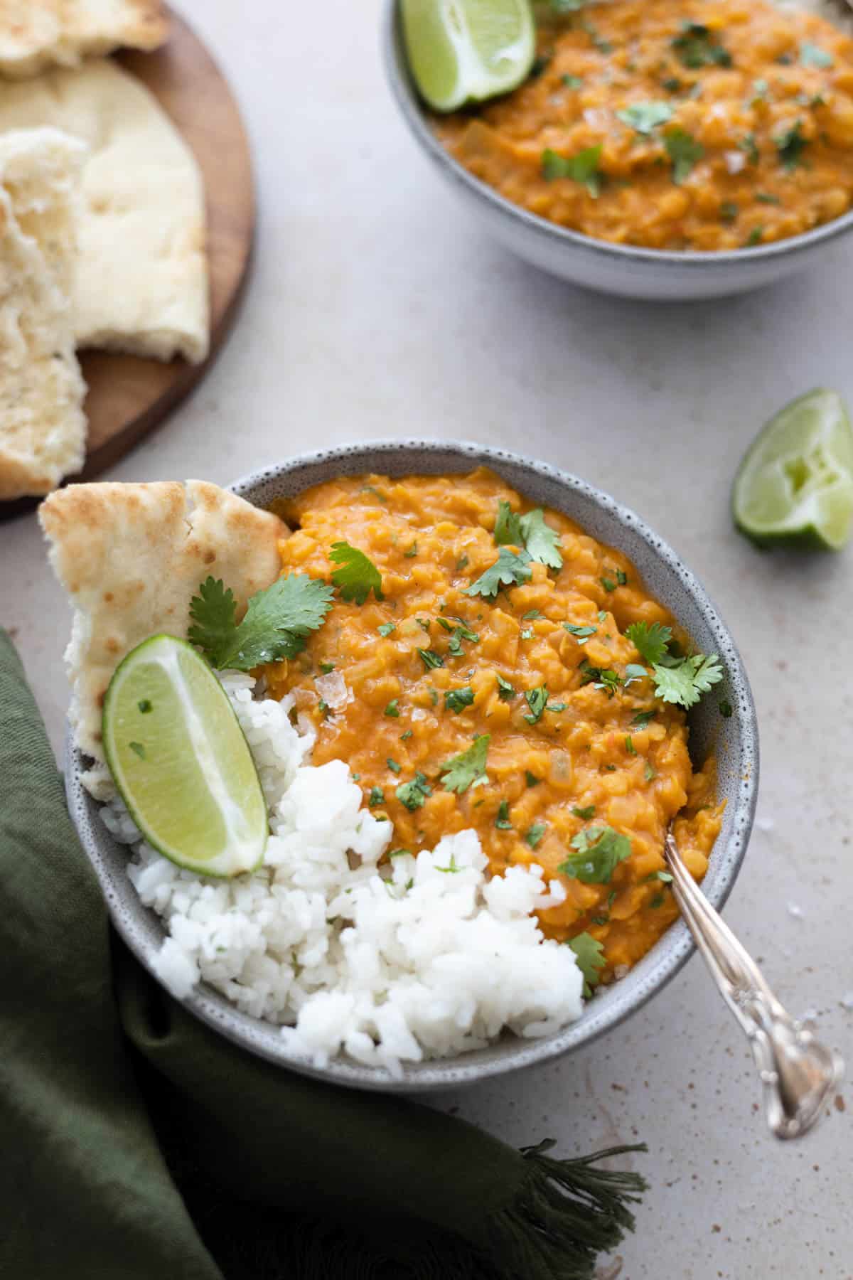 Two bowls filled with red lentil dahl and rice with naan on the side. 