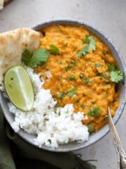 Bowl of red lentil dahl with rice and naan on the side.