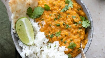 Bowl of red lentil dahl with rice and naan on the side.