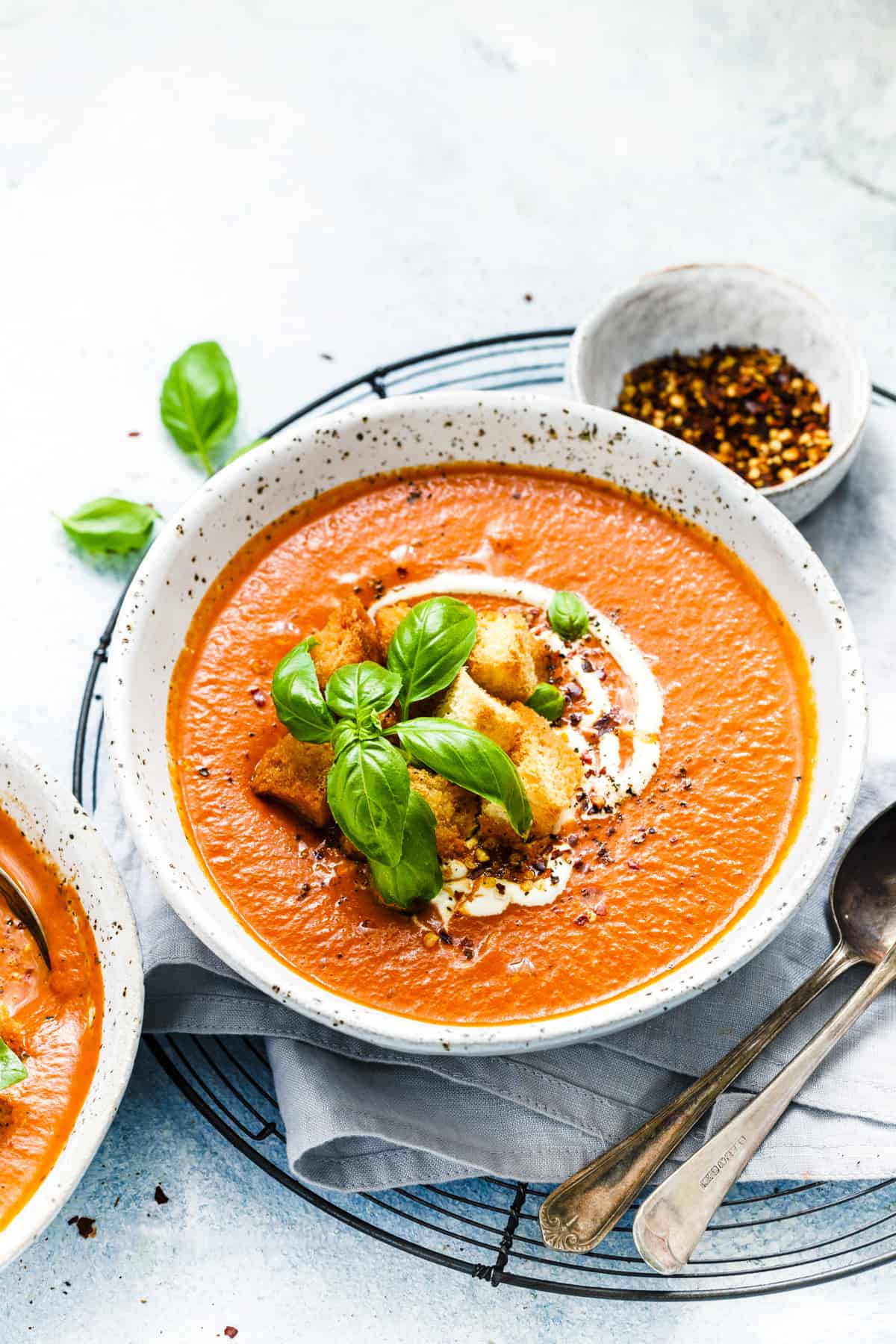 Bowl of tomato soup topped with croutons, basil and cream. Spoons and napkin on the side. 