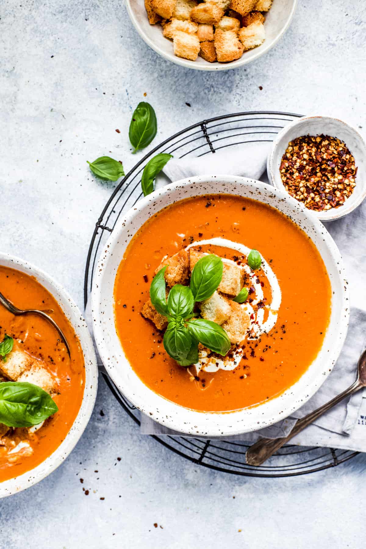 Overhead view of two bowls of soup topped with croutons and fresh basil. 