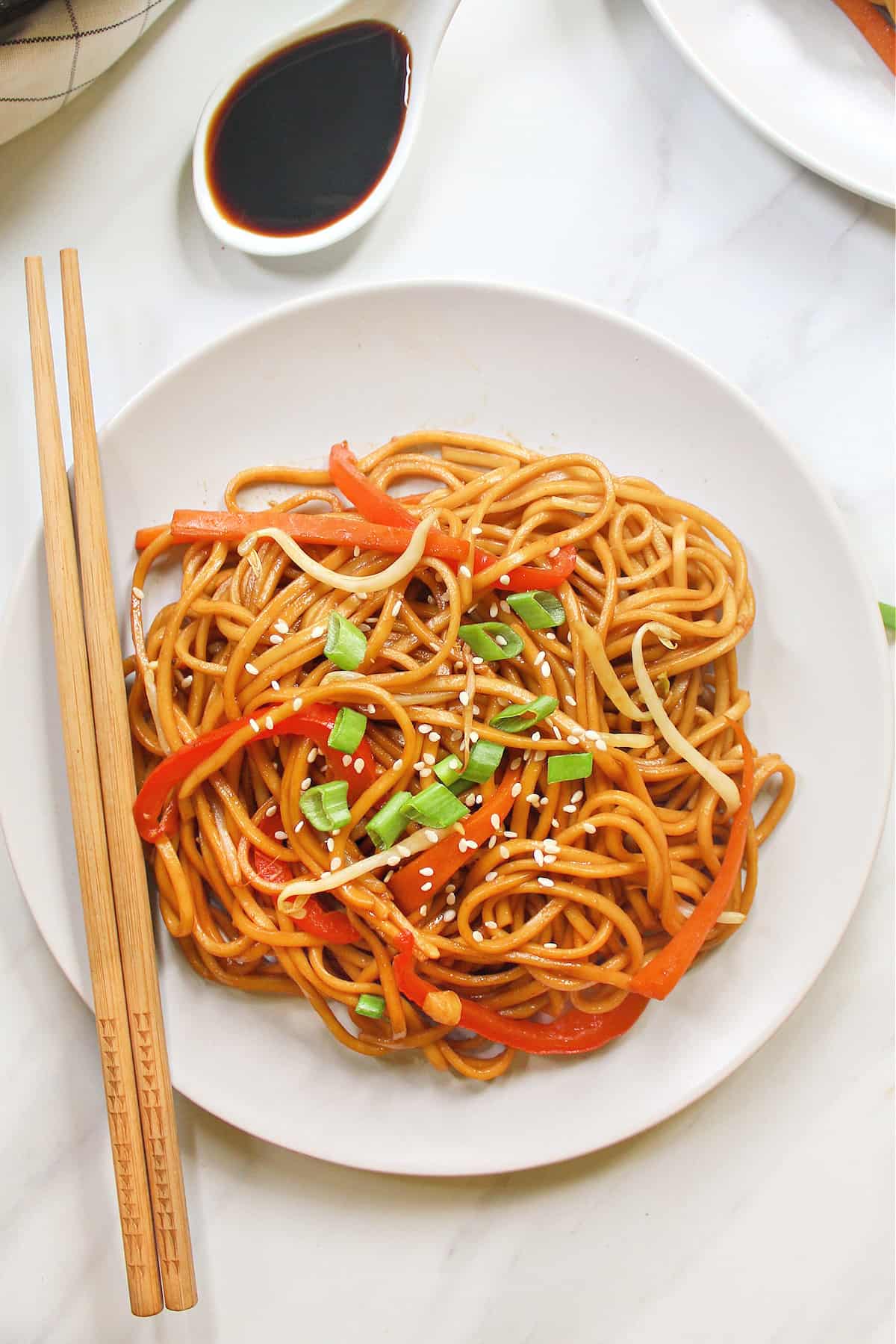 Overhead view of fully cooked vegetable lo mein on a white plate with chopsticks on the side. 