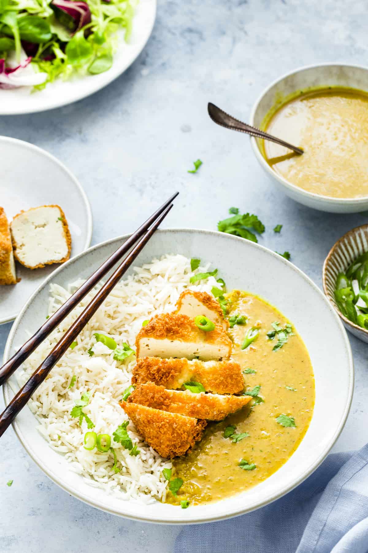 tofu katsu curry in a white bowl with rice on the side. Chop sticks on top of the bowl. 