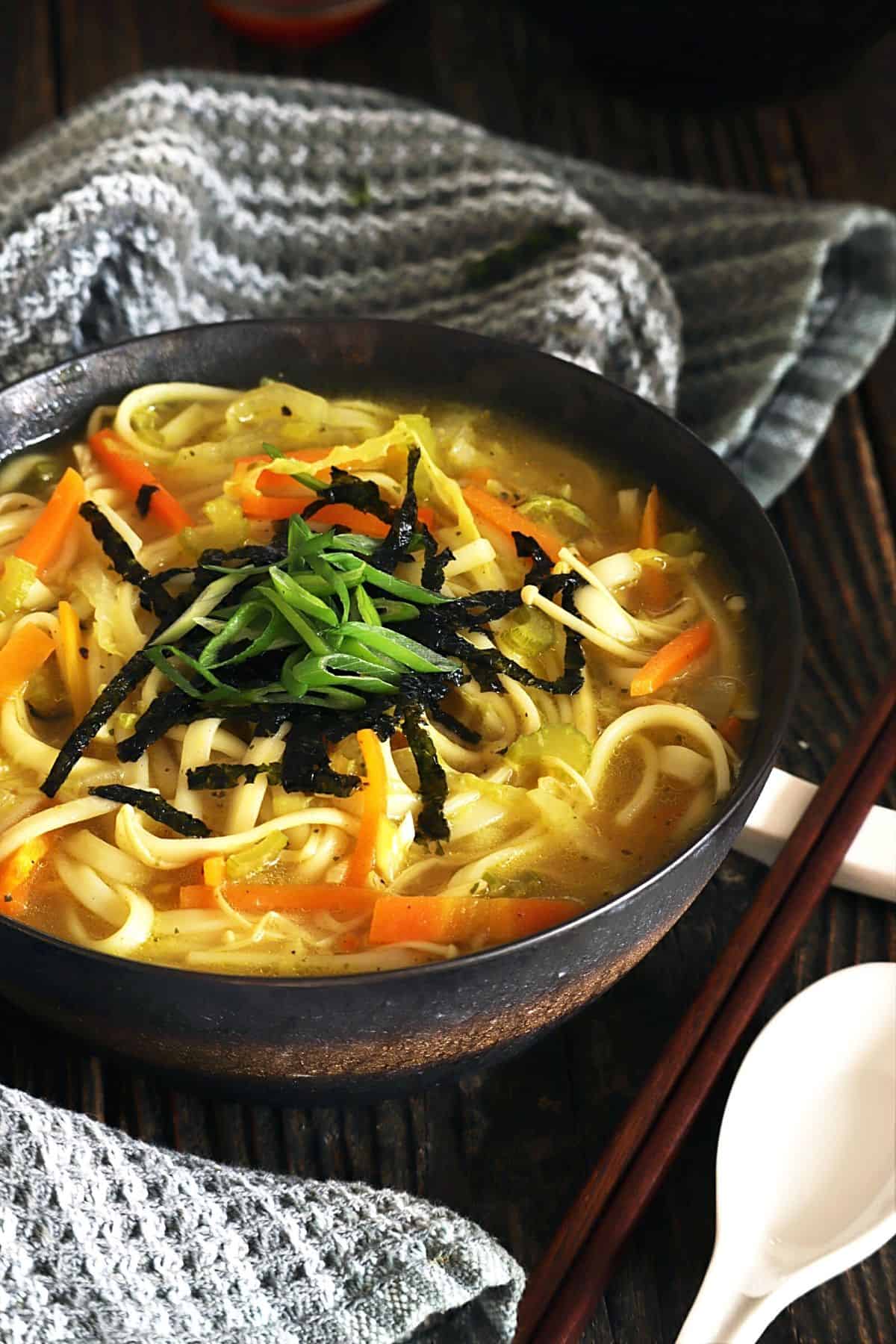 Side view of udon noodle soup in a bowl with chop sticks on the side. 