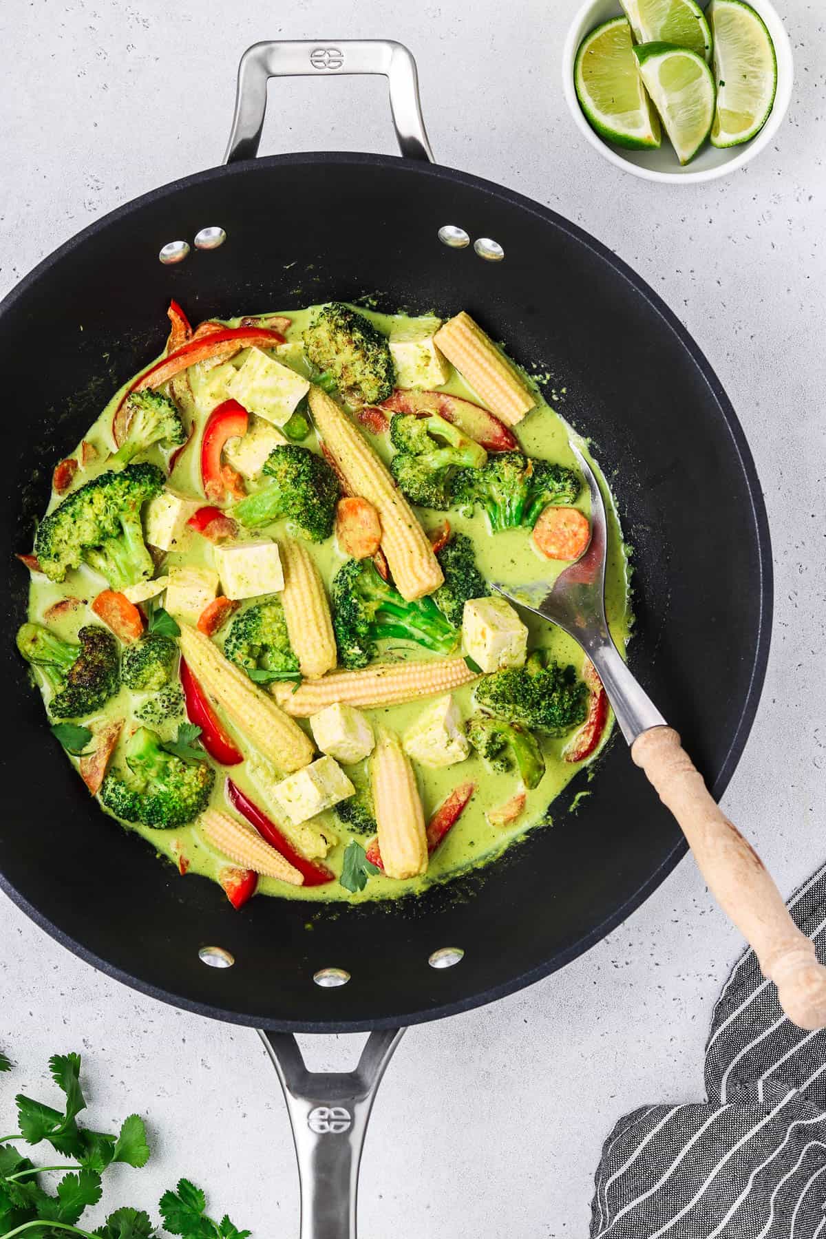 Overhead view of Thai green curry in a wok. Cilantro and lime on the side.