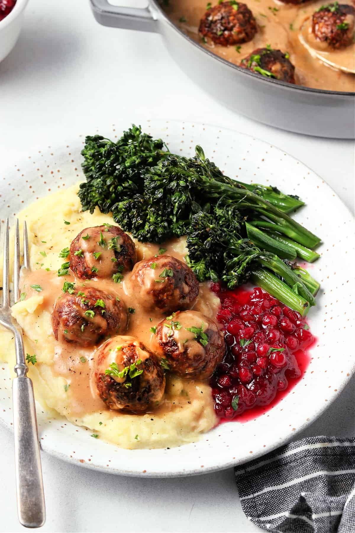 meatballs on a bed of mashed potatoes with gravy on top. Jam and broccoli on the side. 