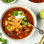 Featured image of vegan tortilla soup on a white table. Cilantro and lime on the side.