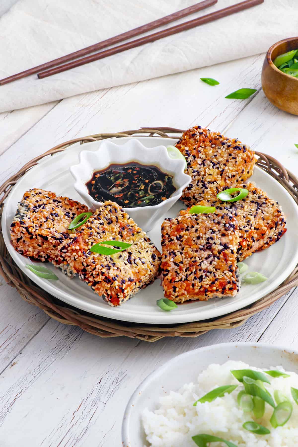 sideview of sesame crusted tofu on a white plate with dipping sauce in the middle. 