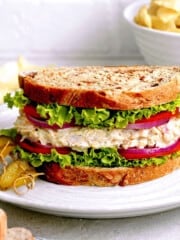 Front view of vegan tuna sandwich on a white plate with pickles on the side.
