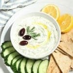 overhead view of tzatziki in a bowl with veggies and pita on the side.