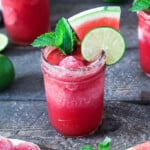 frozen drink in a glass garnished with watermelon, mint and, lime.
