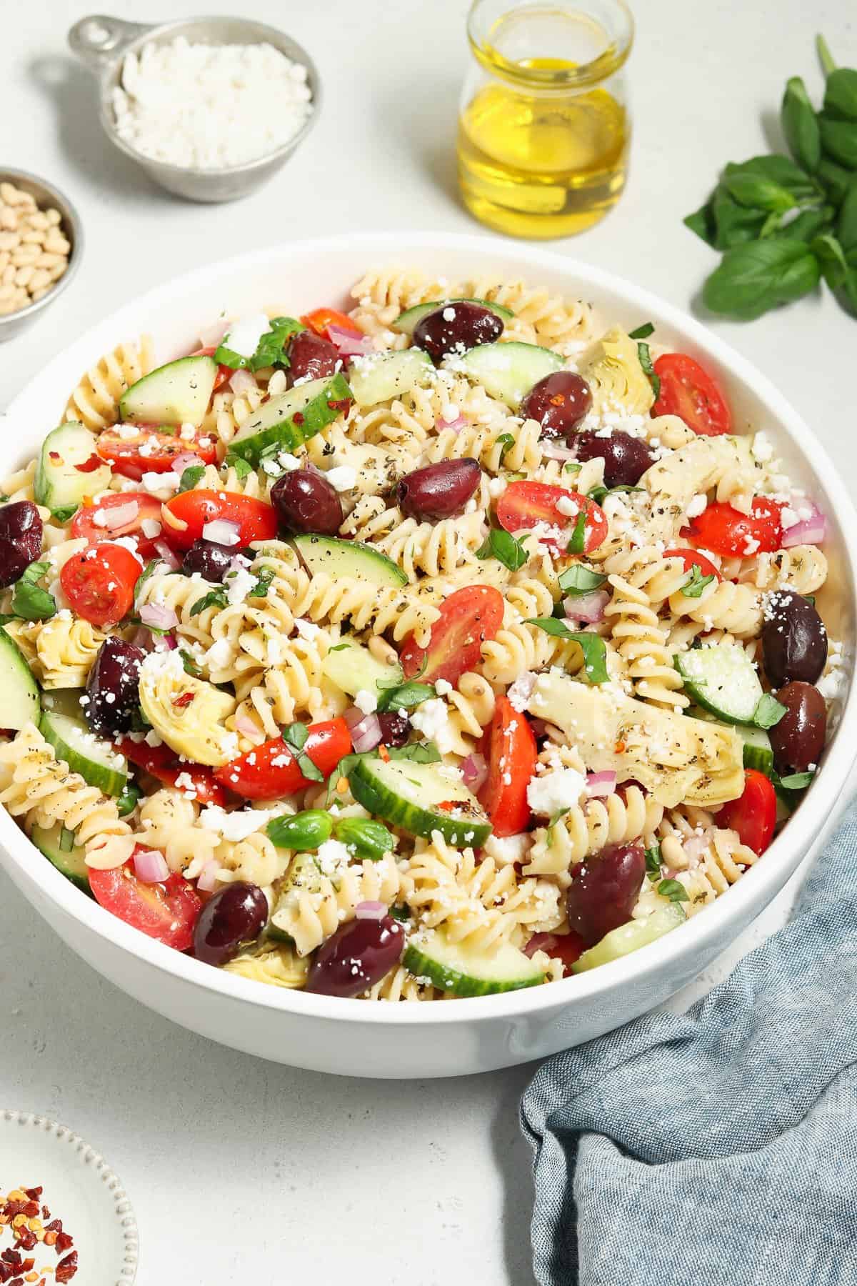 Tossed Mediterranean Pasta Salad in a large bowl. Olive oil, basil and pine nuts on the side. 
