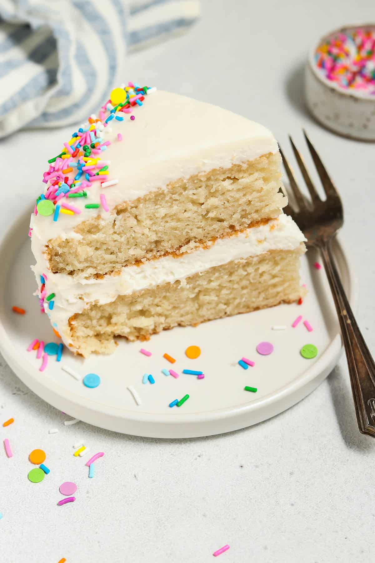 Overhead view of a slice of vegan vanilla cake on a plate. Sprinkles and fork on the side. 