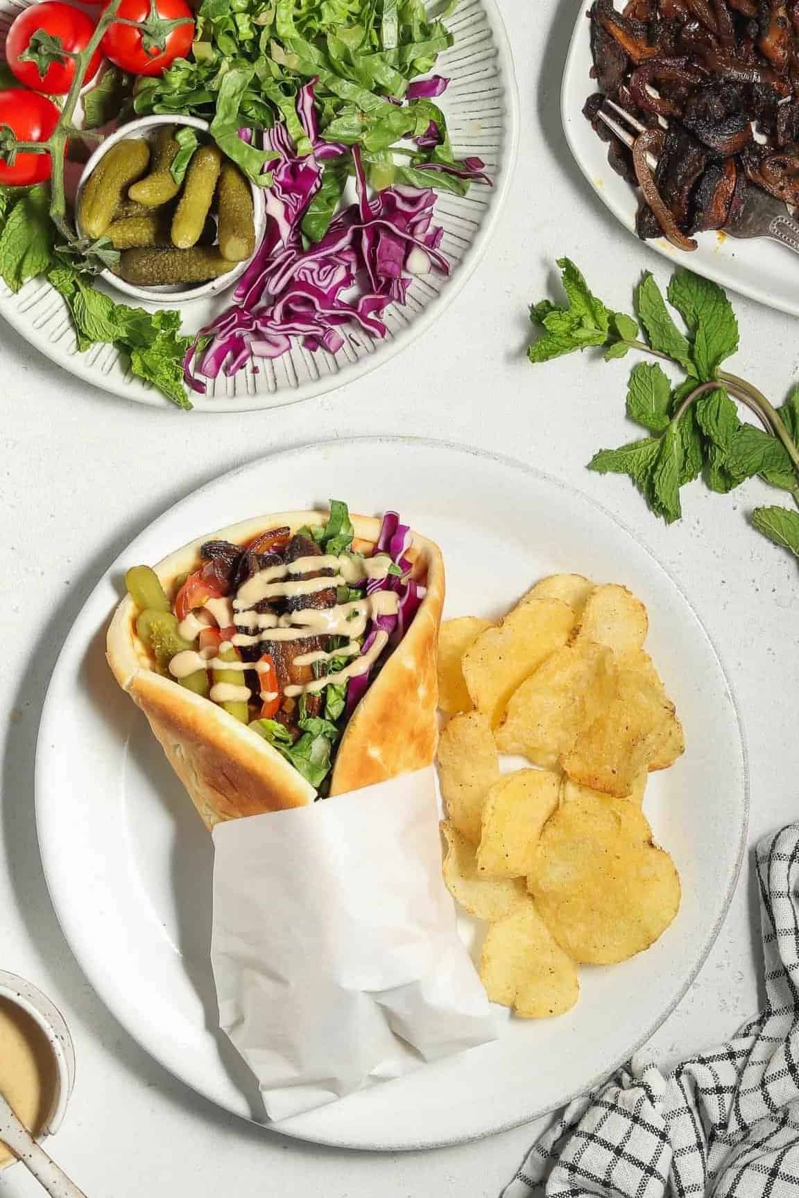 overhead view of a fully assembled mushroom shawarma wrap with a side of potato chips and tahini sauce.