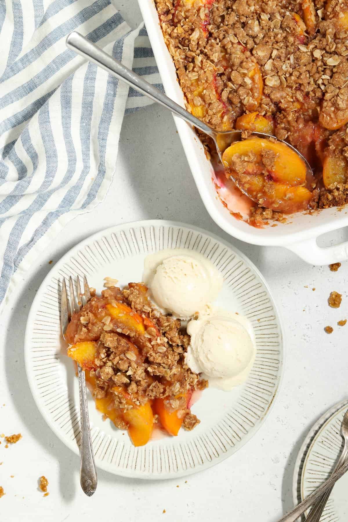 Overhead view of peach crisp and ice cream on a plate. Casserole dish on the side.