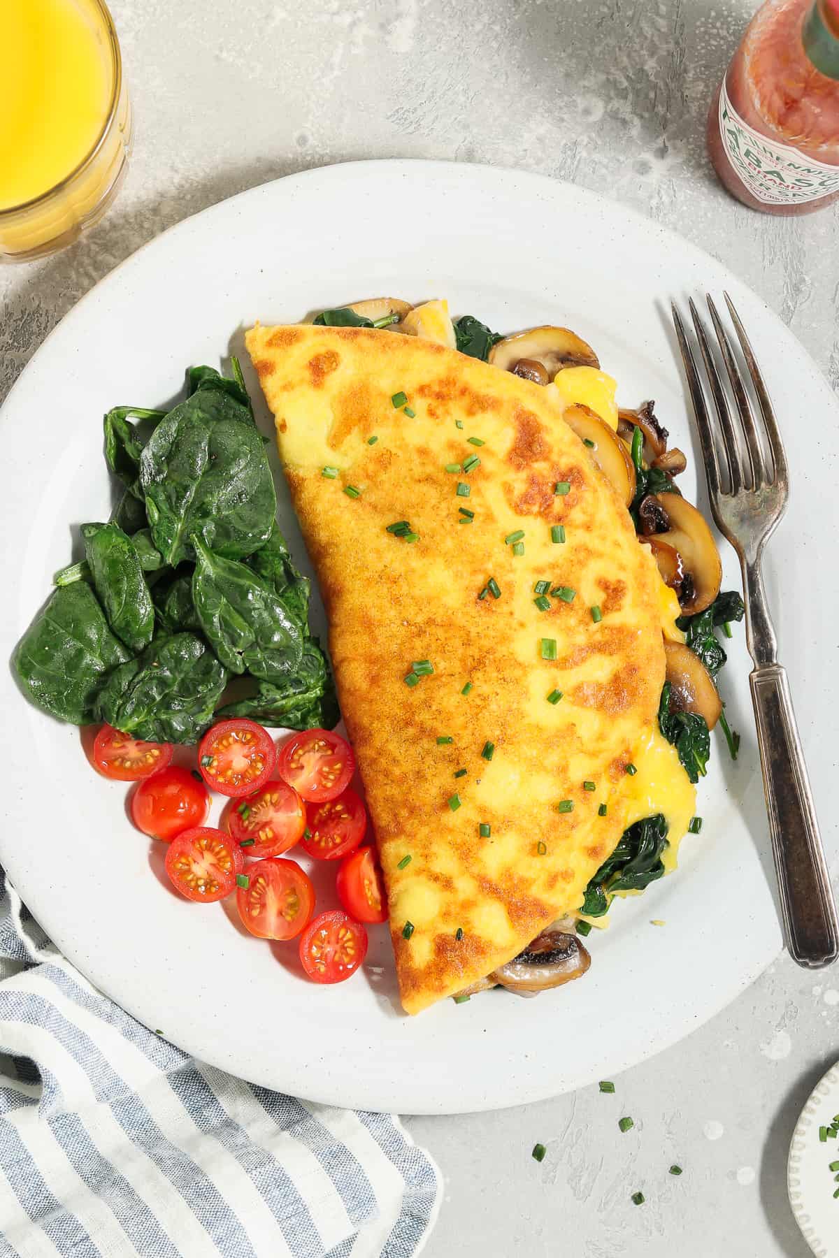 Overhead view of a JUST Egg omelette on a white plate with spinach and tomatoes on the side. 