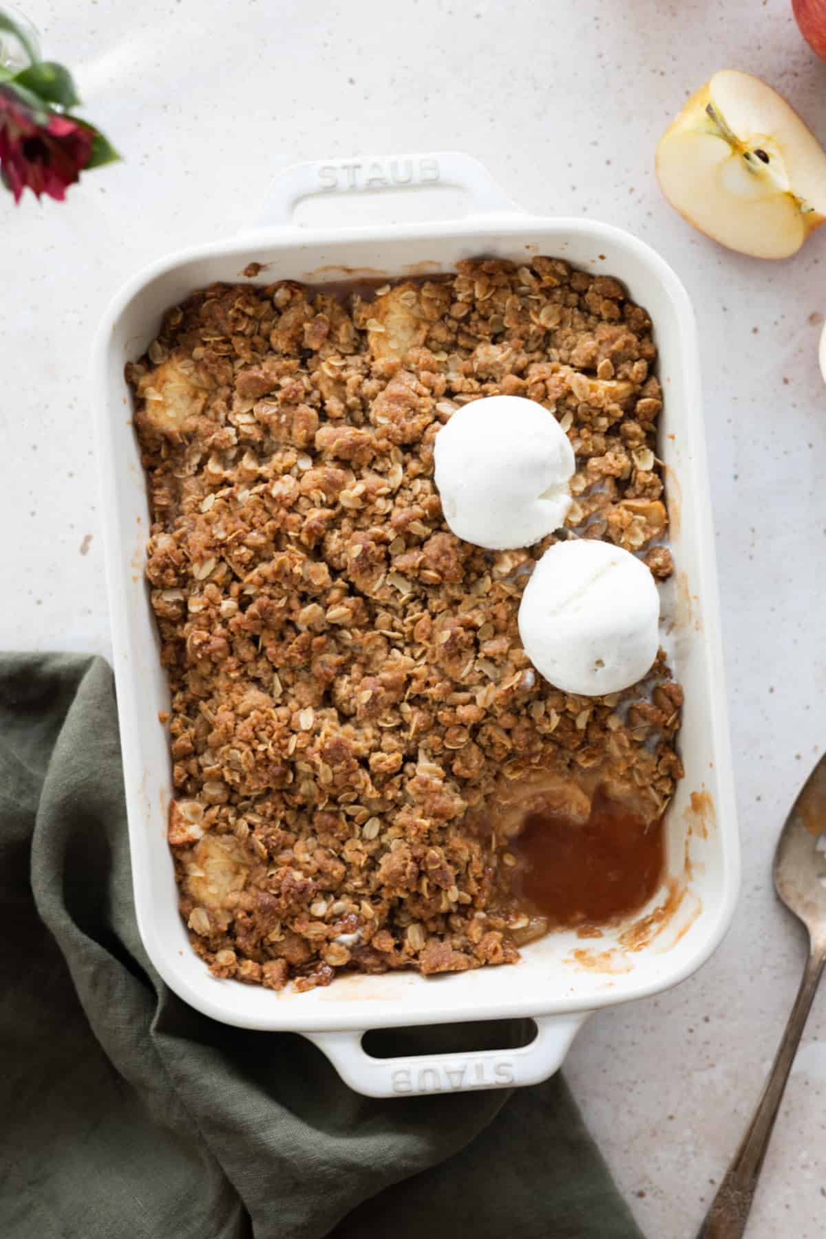 Vegan apple crisp in a casserole dish with two scoops of ice cream on top. 