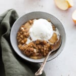 vegan apple crisp in a bowl with a scoop of ice cream on top.