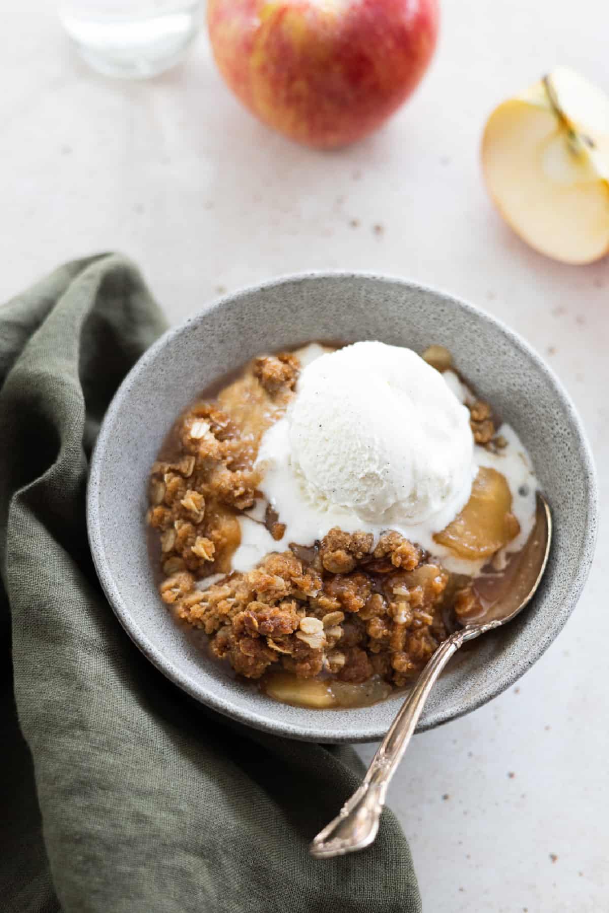 Fully baked vegan apple crisp in a bowl with ice cream on top.
