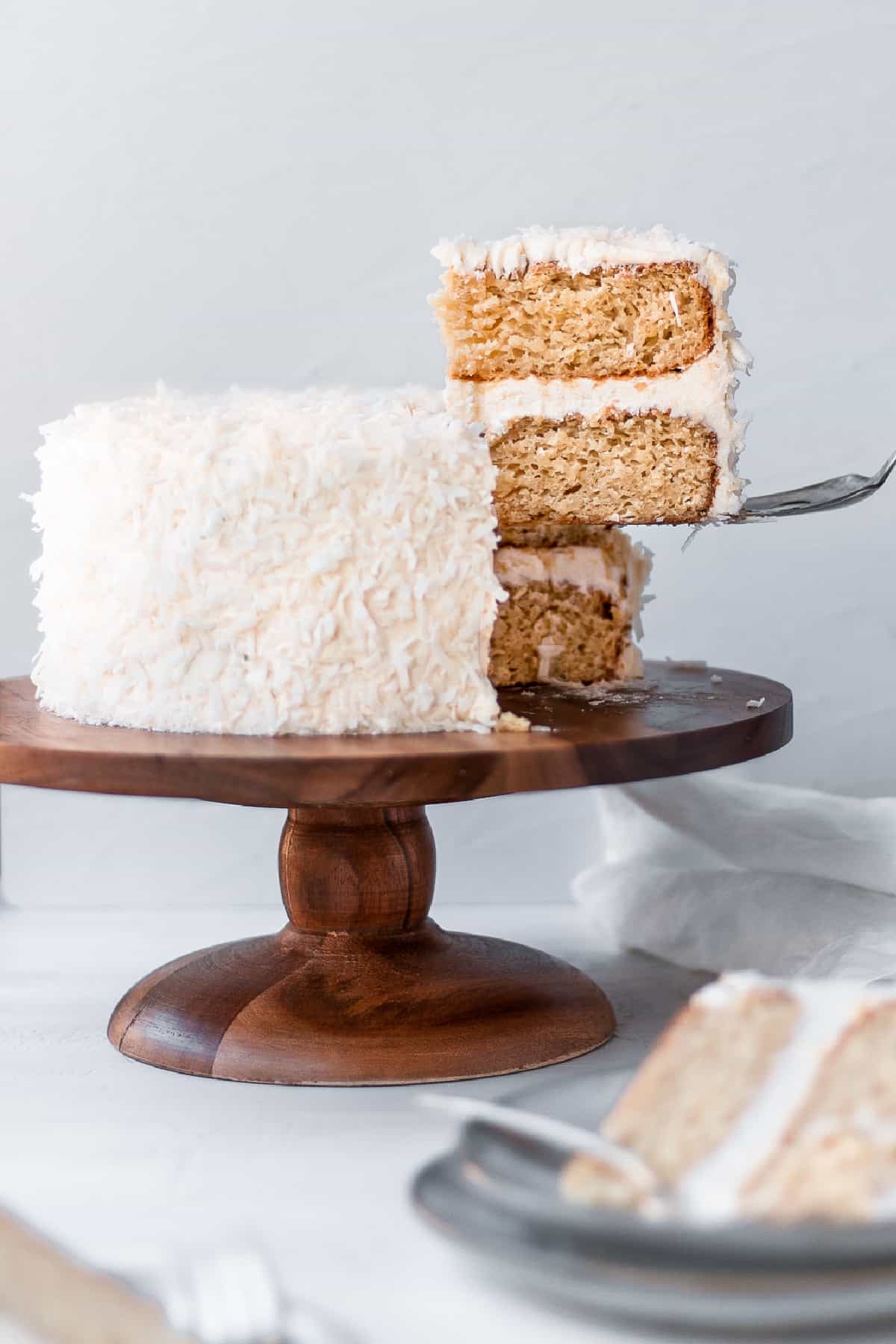 Front view of a vegan coconut cake with one slice being removed with a cake server.