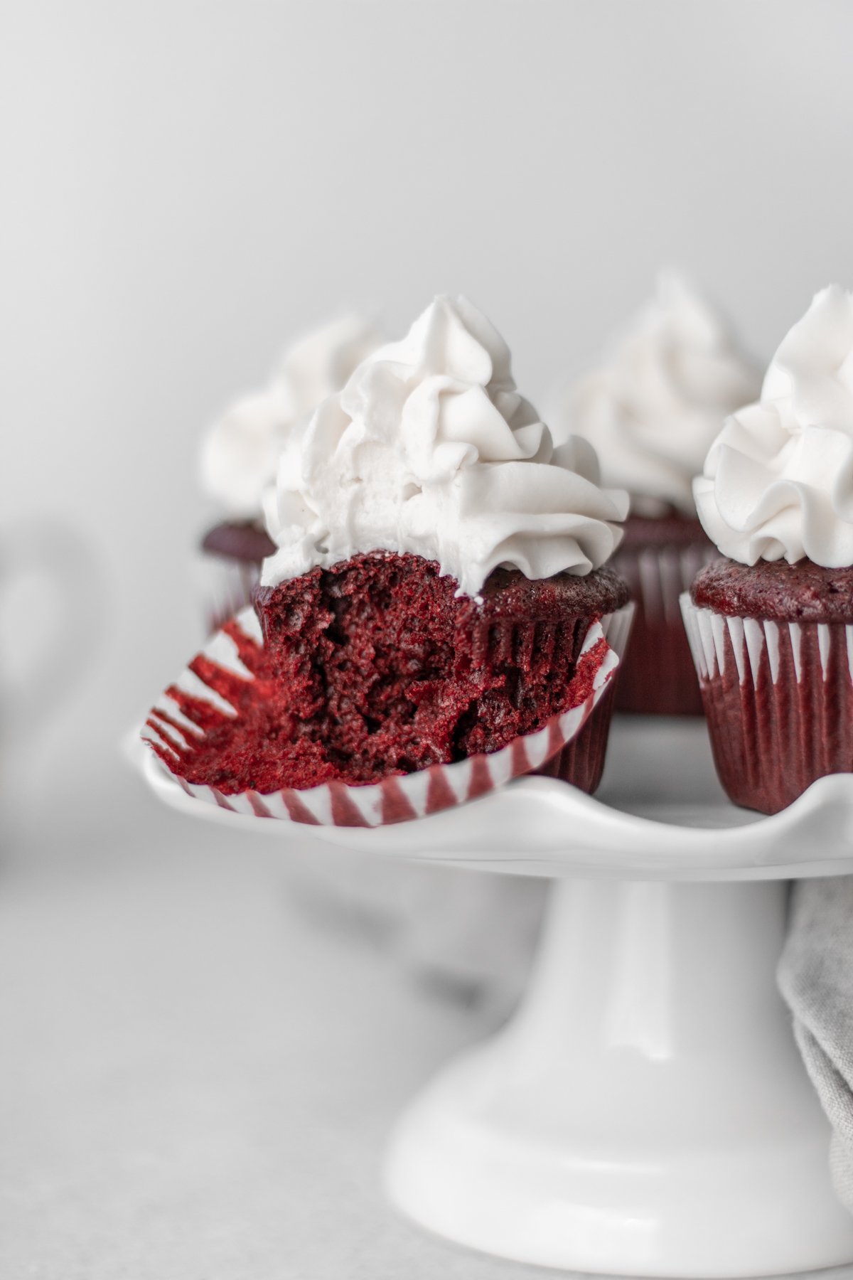 A batch of vegan red velvet cupcakes on a stand with one cupcake's liner pulled back.