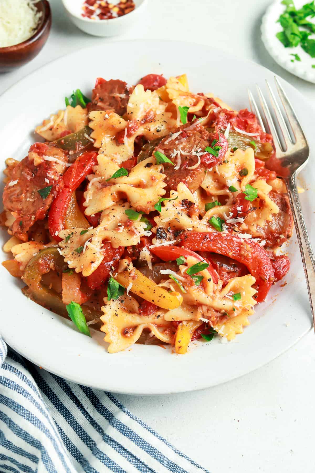 Sausage and peppers pasta on a white plate with a fork on the side. 