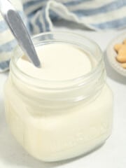 cashew cream in a jar with a spoon inside. Cashews on the side.