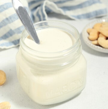 cashew cream in a jar with a spoon inside. Cashews on the side.