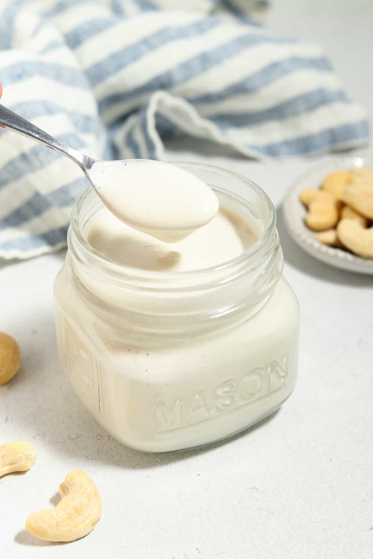 Side view of a spoon being pulled out of a jar of cashew cream.