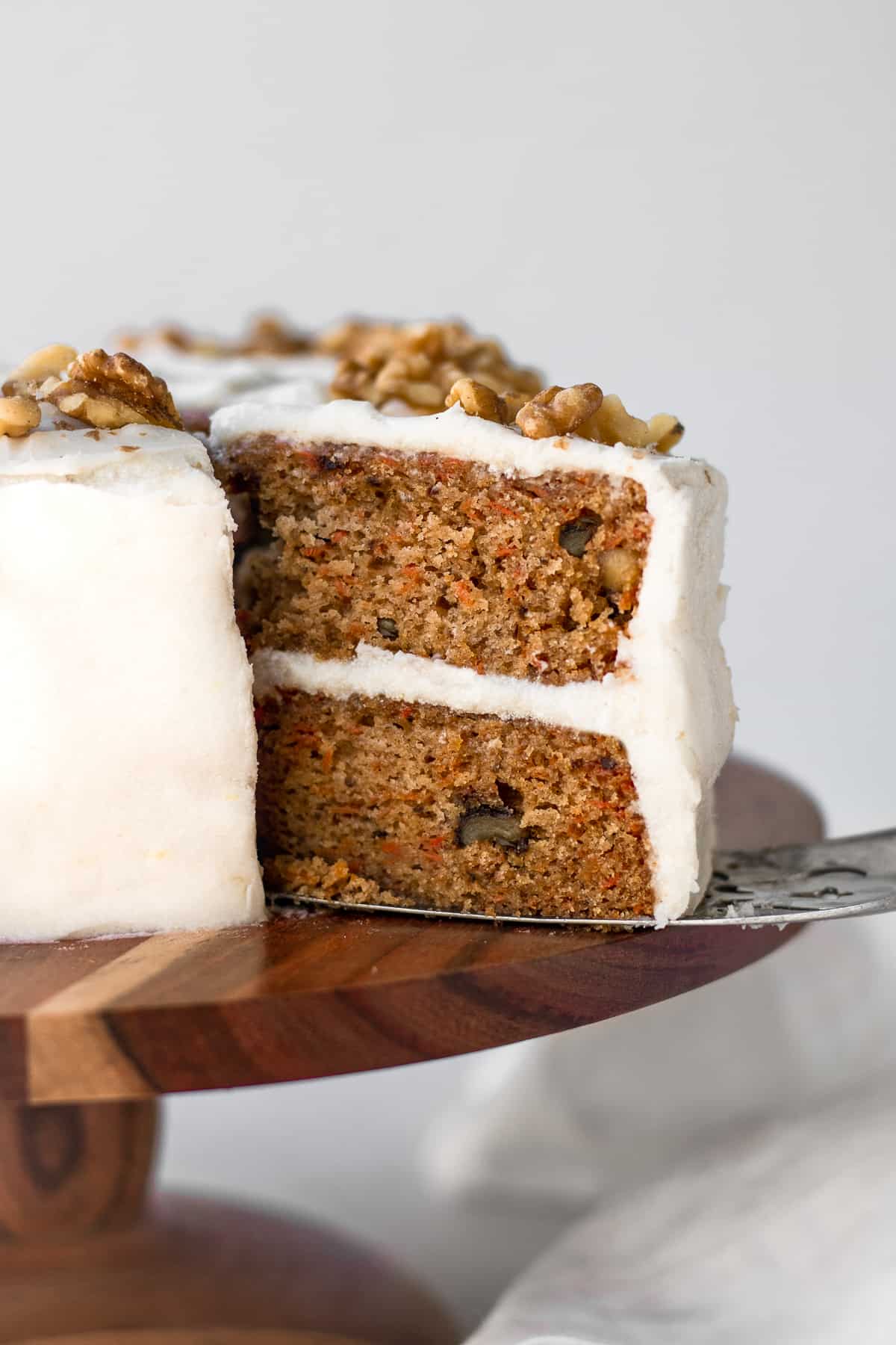 A slice of vegan carrot cake being taken off a cake stand. 