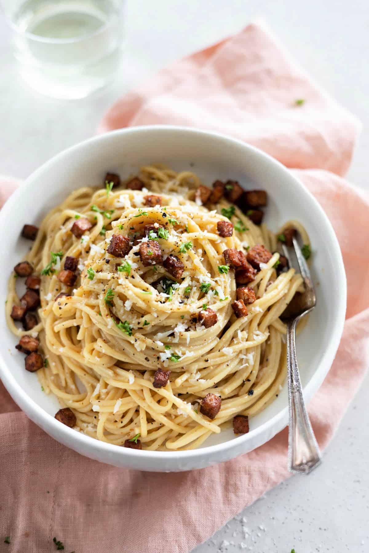 Fully cooked vegan carbonara in a white bowl with fork on the side. 
