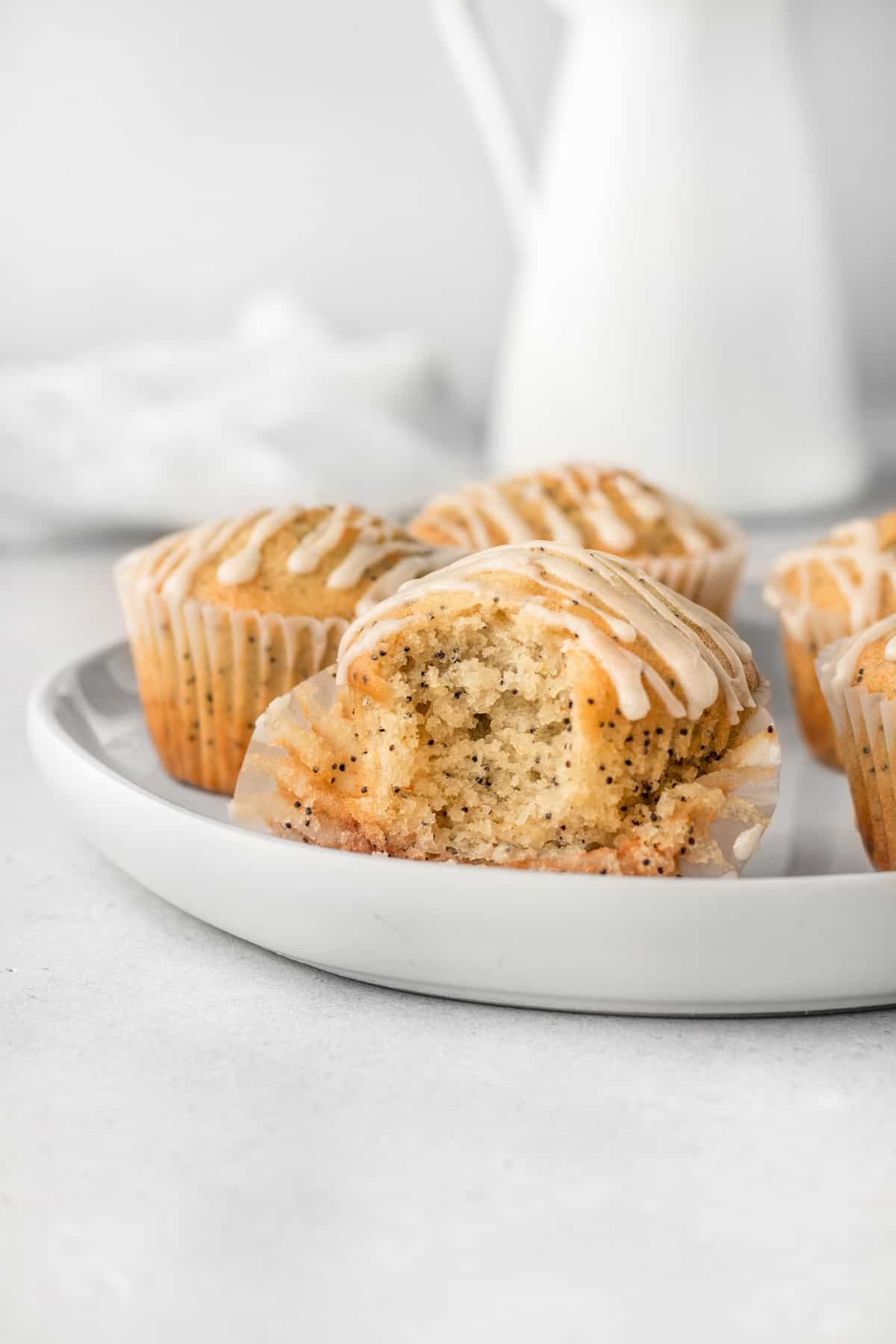 Five lemon poppy seed muffins on a white plate with glaze on top. 
