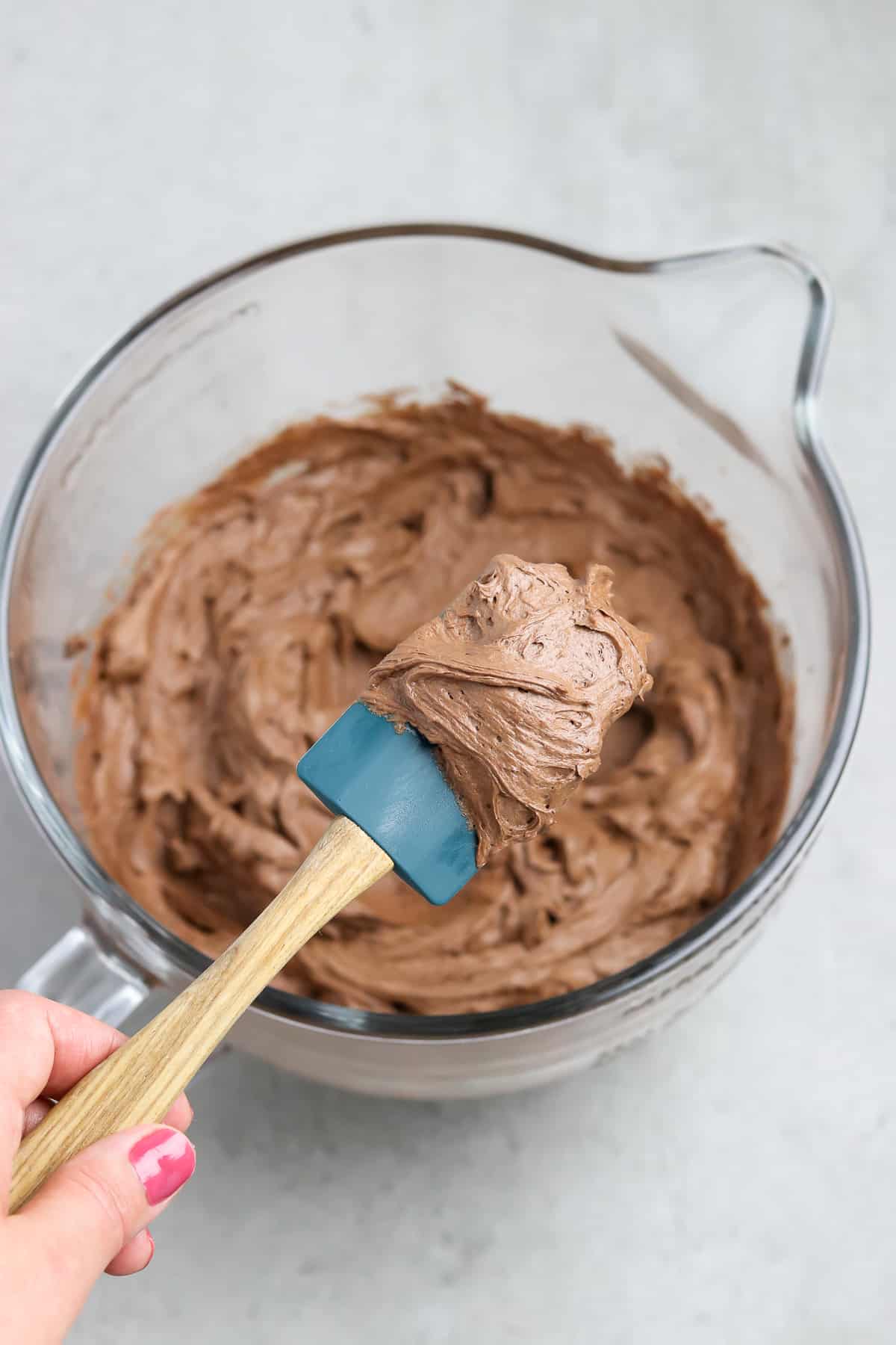 Freshly made vegan chocolate frosting being scooped out with a spatula. 