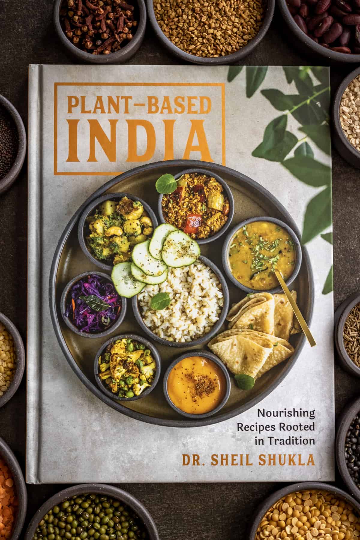 Plant-based India cookbook on a table with spices surrounding it. 