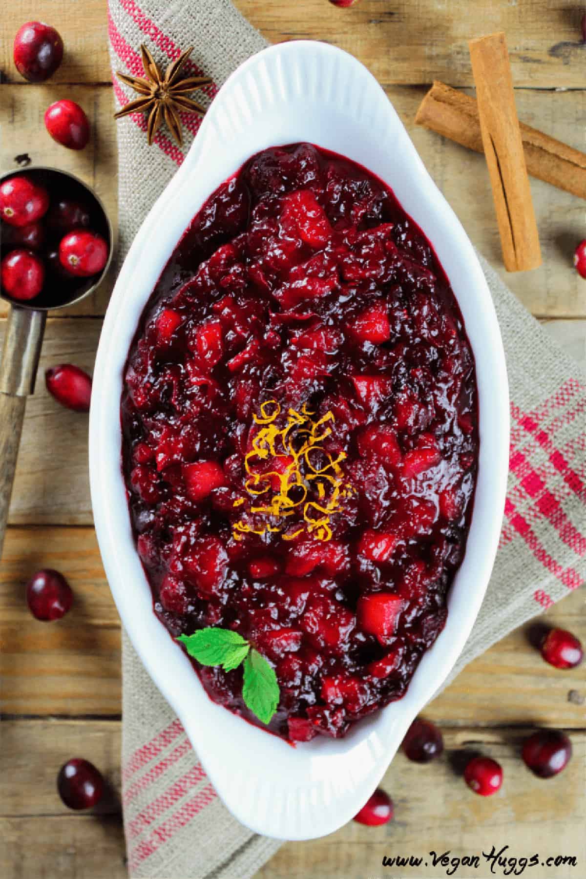 apple cranberry sauce in a white dish with cranberries and cinnamon sticks.